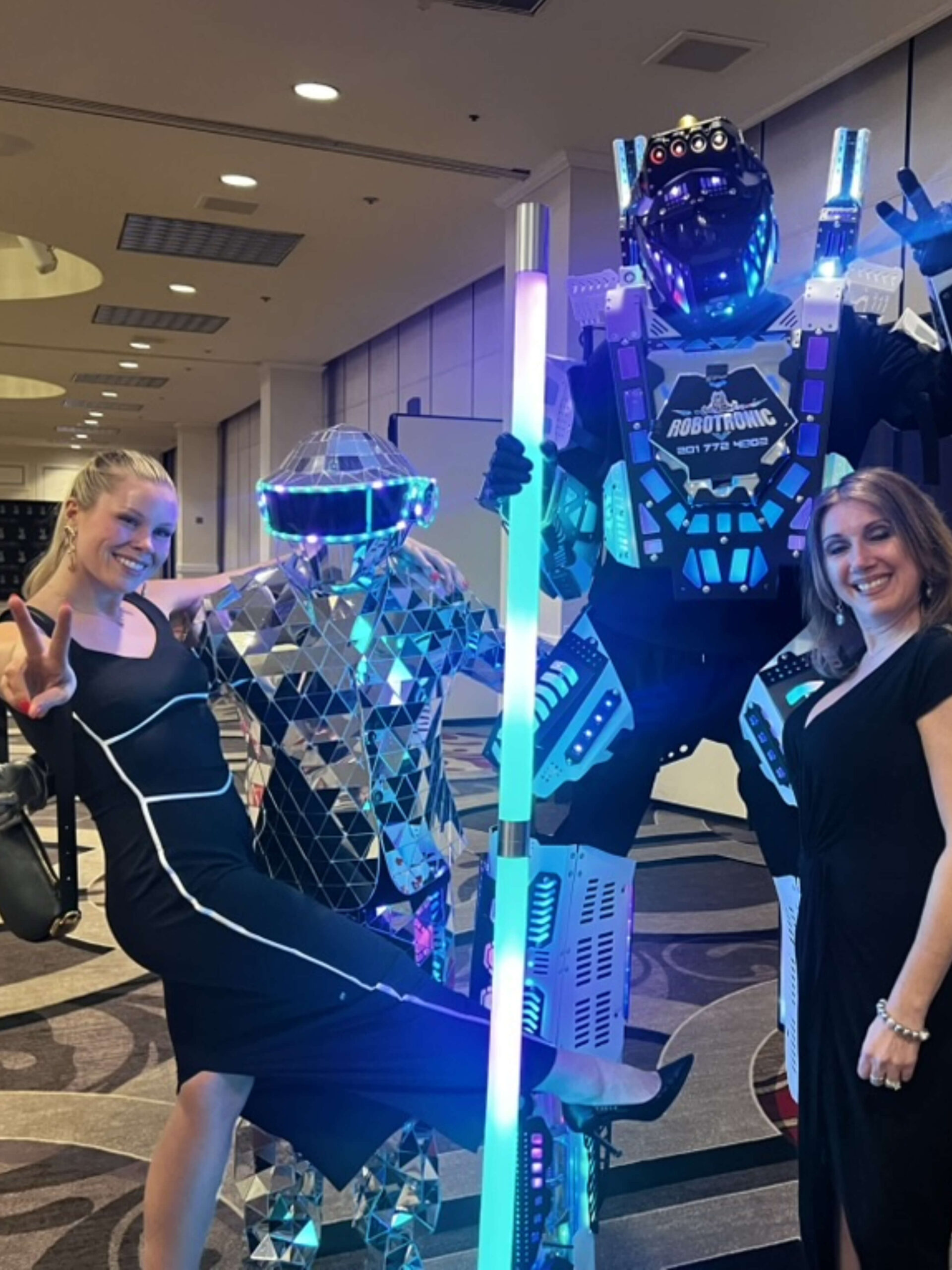 Two women pose with two people in illuminated robot costumes at the ICA Spring Gathering Guides event, with one woman making a peace sign and the other smiling. - Intercoiffure Canada America