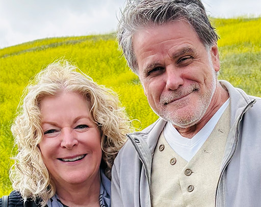Two older adults, a woman and a man, stand outdoors in front of a green field, smiling at the camera during the 2026 Spring Regional—capturing a moment of McGaha Magic for this event preview. - Intercoiffure Canada America